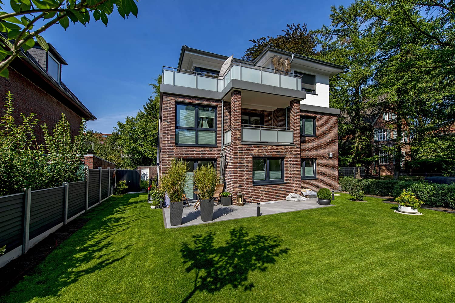 Modernes Haus mit großem Rasen und gepflegtem Garten, umgeben von einer einladenden Landschaft.